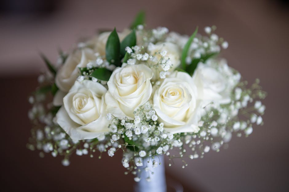 A bouquet arrangement featuring creamy white roses with gently unfolding petals, accented by delicate sprigs of baby's breath with tiny white flowers and green leaves, all arranged in a compact, round