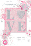 This anniversary card appears like a small, romantic artwork, ideal for accompanying a bouquet delivered across Upminster on a special day. At its heart sits the word LOVE, boldly centred in tall, raised letters that have been dusted with soft pastel glitter in blush pink, pearlescent white, and fine silver touches. The texture is distinctly embossed and slightly rough to the touch, giving a satisfying sense of depth, as if the word has been lovingly carved out of light. The letter O is subtly shaped to feel especially rounded and inviting, drawing the eye and hand alike. Behind and around this focal point stretches a gentle wash of pale pink, deepening in places to create a hazy, almost dreamlike glow reminiscent of dawn light over the rooftops near Upminster station. Encircling the center, a trail of stylised blossoms and leafy vines curves gracefully outward. These flowers are depicted with delicate outlines and soft shading in blush, mauve, ivory, and gentle grey, with occasional silver highlights on petals and leaves, like dew drops catching the early sun. Their flowing lines echo the natural movement of stems in an English garden, the kind you might see translated into a fresh anniversary bouquet in a local Upminster florist. Tiny curls, petals, and barely-there butterflies are woven into the pattern, adding a sense of motion and intimacy without clutter. Inside, in a refined, understated script, appear the words On Our Anniversary and I love you today and always, set with ample space so the sentiment feels calm and sincere. The card radiates tender celebration, ideal for marking another year of shared life in a cosy Upminster home, with flowers and memories close at hand.